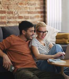 A man and a woman are sitting on a couch with a laptop on a table in front of them.
