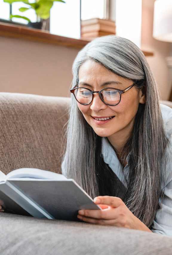 A person is reading a book on a grey couch.