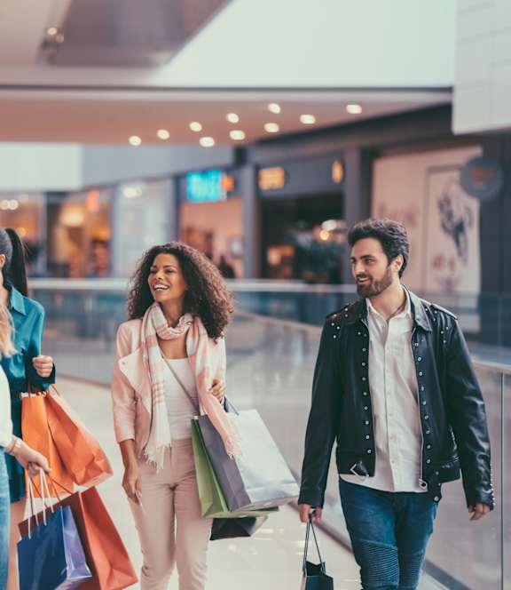Four people walking in a mall carrying shopping bags.