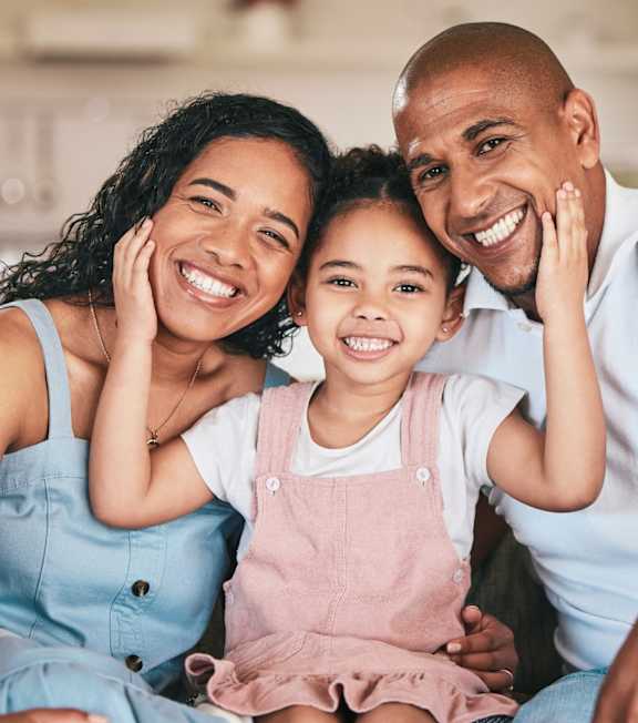 A family of three is sitting closely together on a couch.