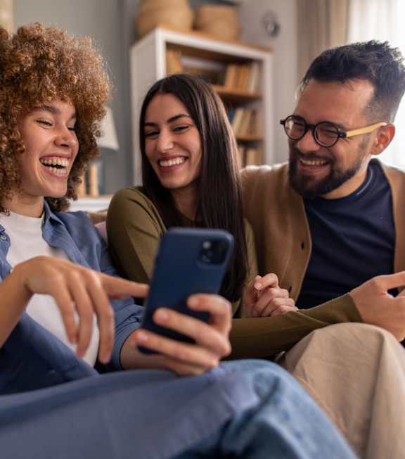 Three people are sitting on a couch, looking at a smartphone.