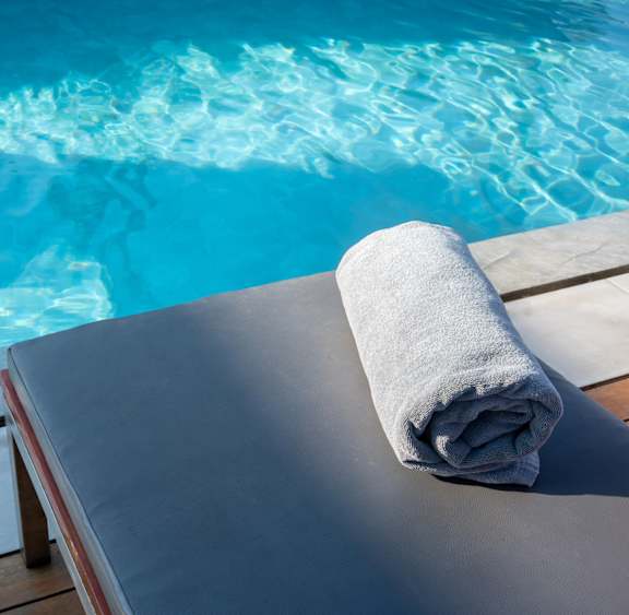A towel is rolled up and placed on a lounge chair by a pool.