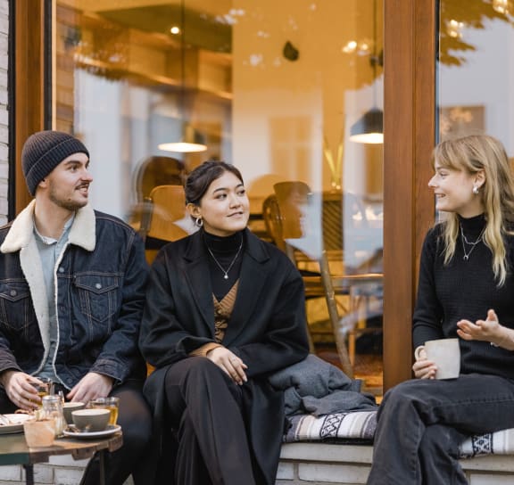 three people sitting on a bench in front of a coffee shop