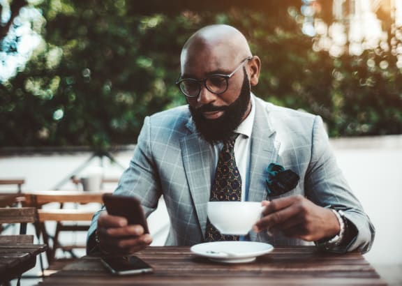 a man sitting at a table with a cup of coffee and looking at his phone at Claret Village at LaFayette Trail, Tallahassee, 32311