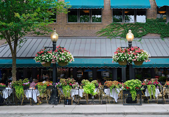 A restaurant with tables and chairs under flower baskets.