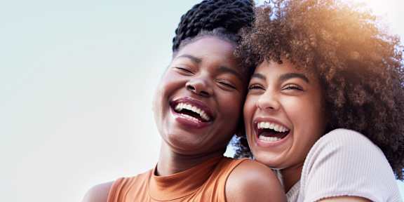 Two women laughing together with one wearing an orange top.