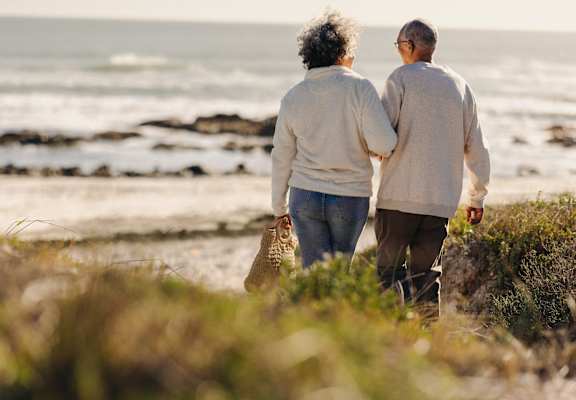 An elderly couple walking hand in hand on a beach.