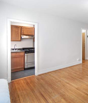 an empty living room with wood flooring and a kitchen