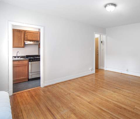 an empty living room with wood flooring and a kitchen