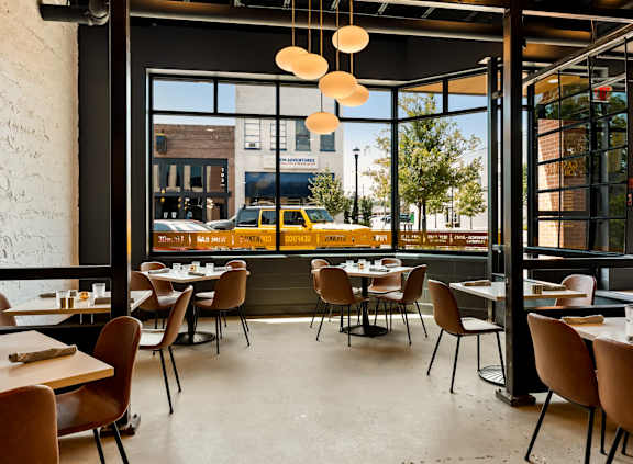 A restaurant with tables and chairs and a view of the street outside.