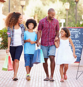 A family of four walking down a sidewalk holding hands.