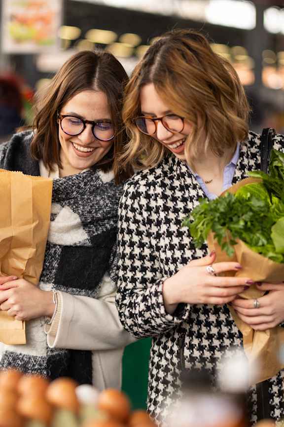 Two women shopping for vegetables in a grocery store.