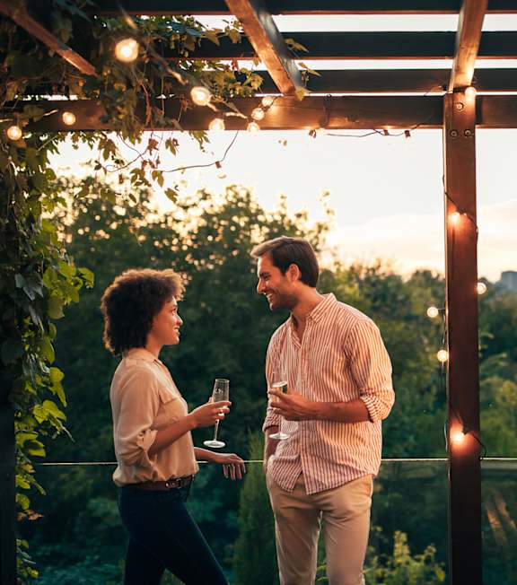 Two people standing under a pergola with string lights.