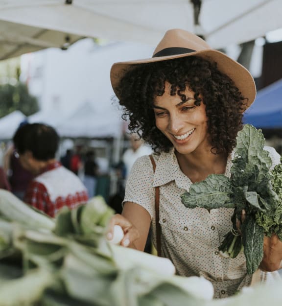 a woman in a cowboy hat holding a bunch of broccoli at a farmers market at The Madison, Columbus, OH, 43215