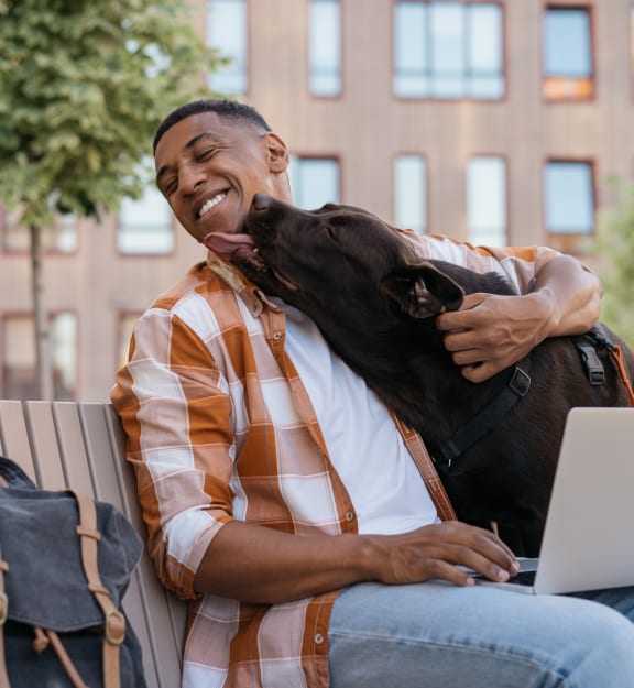 a man sitting on a bench with his dog and a laptop at Renaissance Park Apartments, California, 95618