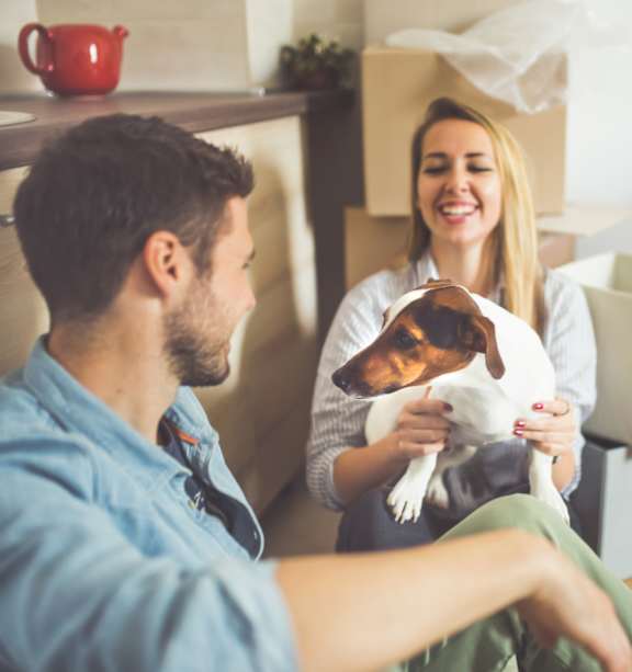 A man and woman sitting on the floor with boxes around them, the woman is holding a dog at The Madison Apartments and Townhomes, Georgia 30044