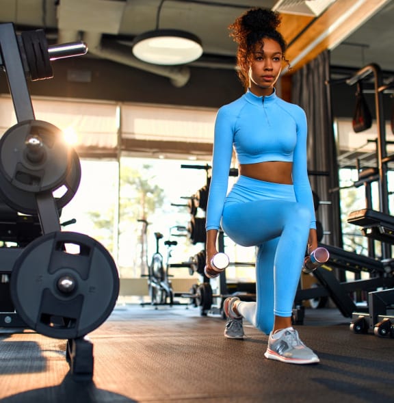 a woman in a blue body suit squats in a gym with weights