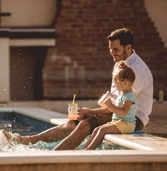 A man and a child are sitting by a pool.