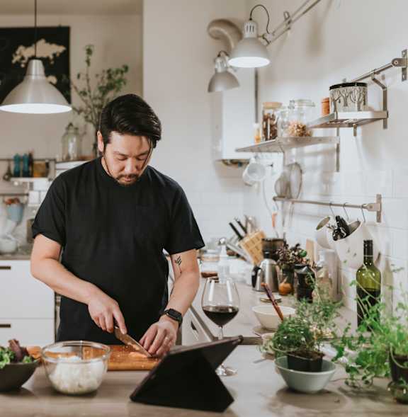 A man is cutting vegetables on a cutting board in a kitchen.