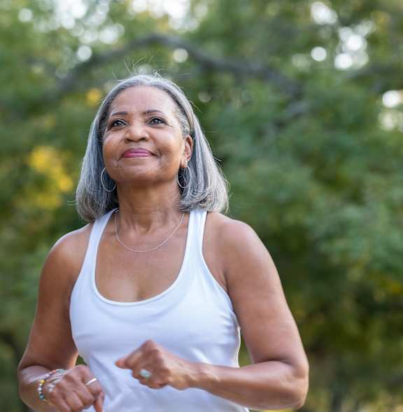 A woman in a white tank top is running outdoors.