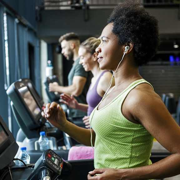 A woman in a green tank top is working out on a treadmill in a gym.