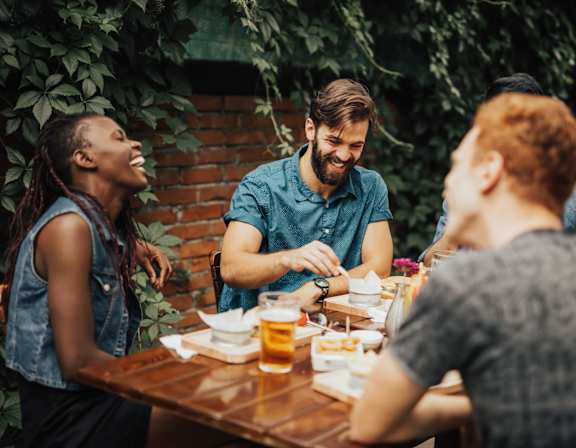 Group of people are sitting around a wooden table, enjoying food and drinks1 at AMP 30 Apartments, San Diego, California