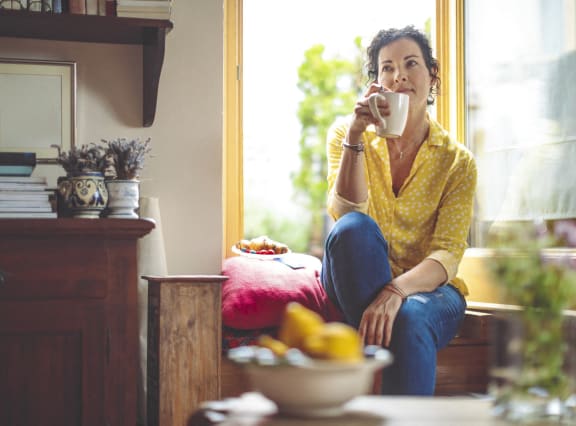 a woman sitting on a window sill drinking a cup of coffee