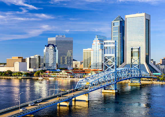 A city skyline is reflected in a lake with a building in the foreground.