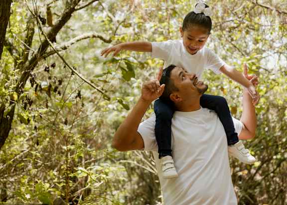 A man lifts a child into the air in a forest.