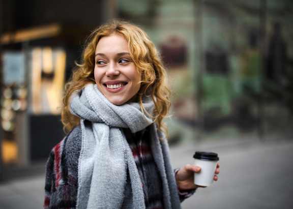 A woman with curly hair is holding a cup and wearing a scarf.