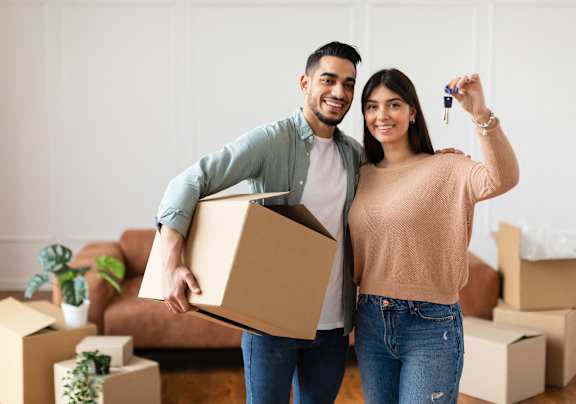 A man and woman are standing in a room with boxes, holding a key and a box.