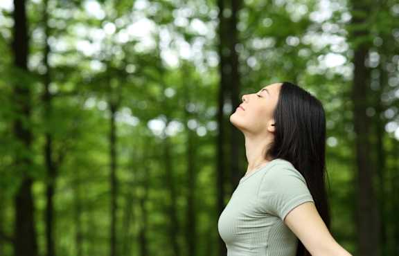 A woman with long black hair is standing in a forest.