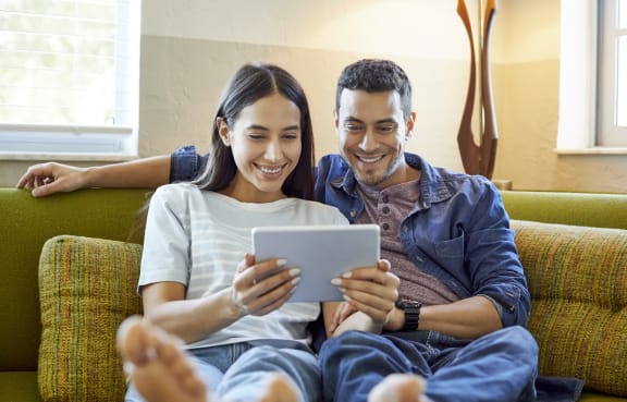 Couple Sitting on Couch Together Browsing on Tablet at Thornberry Woods Apartment Homes in Naperville, IL, 60565