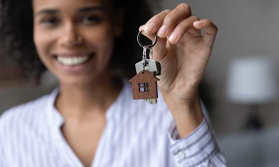 A woman holding a keychain with a house-shaped pendant.