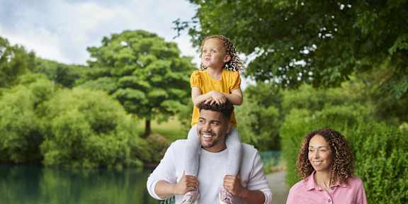 A man carries a child on his shoulders while walking with a woman.