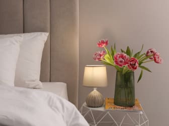 a vase of flowers on a nightstand next to a bed