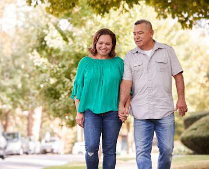 An older couple holding hands and walking down a tree-lined street.