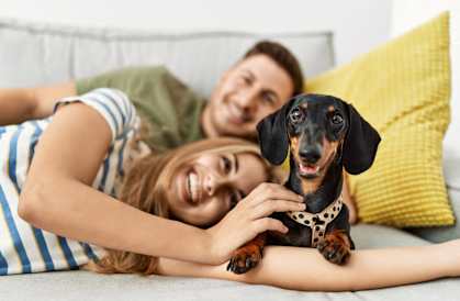 two people laying on a couch with a dog