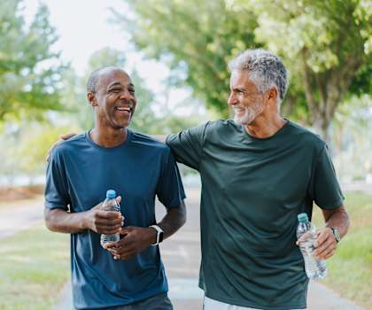 Two men are walking and talking in a park.