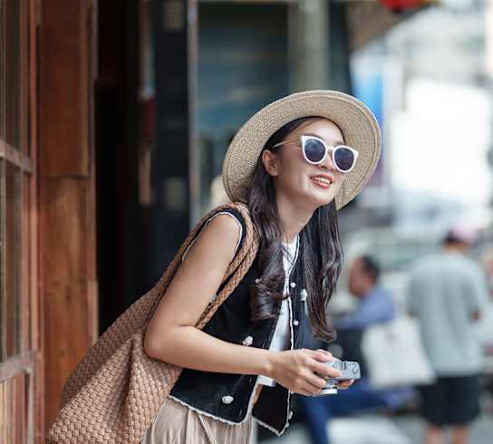 A woman in a hat and sunglasses is looking at her phone.