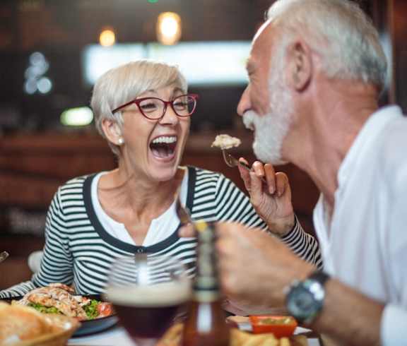 an older couple laughing while eating food at a restaurant