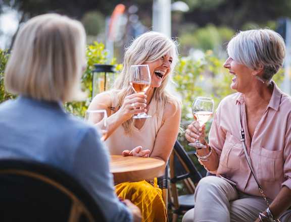 three women sitting at a table laughing and drinking wine