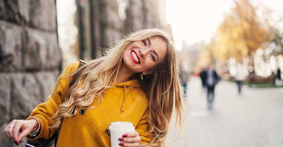 A woman in a yellow hoodie is holding a cup and smiling.