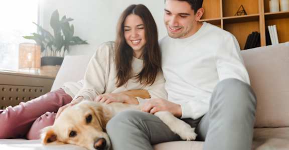A man and woman are sitting on a couch with a dog between them.