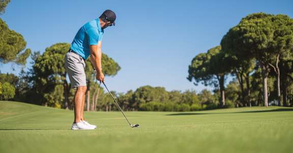 A man in a blue shirt and white shorts is playing golf on a sunny day.