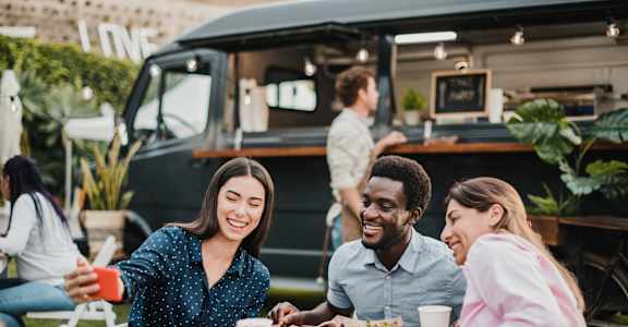 Three people are sitting at a table enjoying food and drinks in an outdoor setting at Kiwi Goji Apartments, TN, 38111