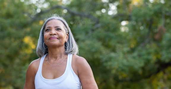 A woman in a white tank top is running outdoors.