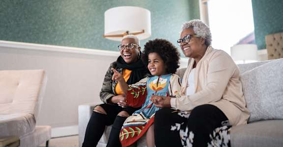 Three people are sitting on a couch in a living room.