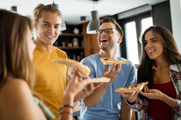 Three people are sitting at a table eating pizza and drinking soda.
