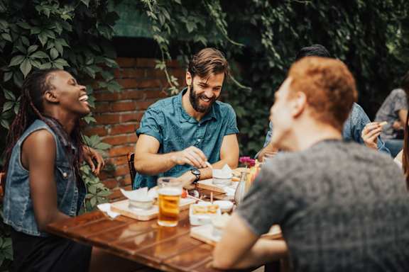 Group of people are sitting around a wooden table, enjoying food and drinks at AMP 30 Apartments, San Diego, CA, 92116